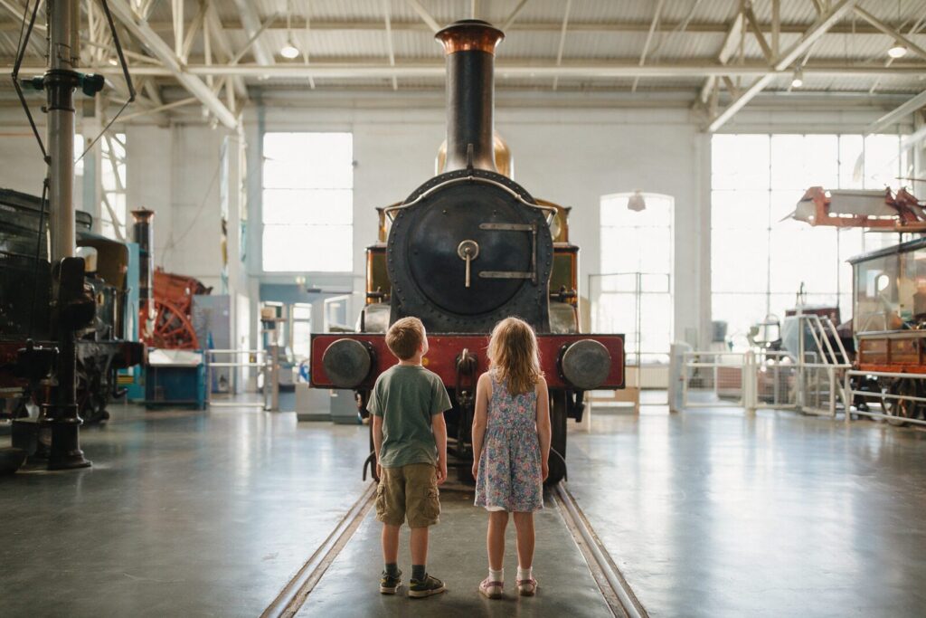 Zwei Kinder bestaunen eine historische Dampflokomotive in einem Verkehrsmuseum