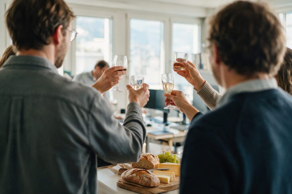 Team st&ouml;sst bei einem Ap&eacute;ro im B&uuml;ro mit Brot, K&auml;se und Trauben an